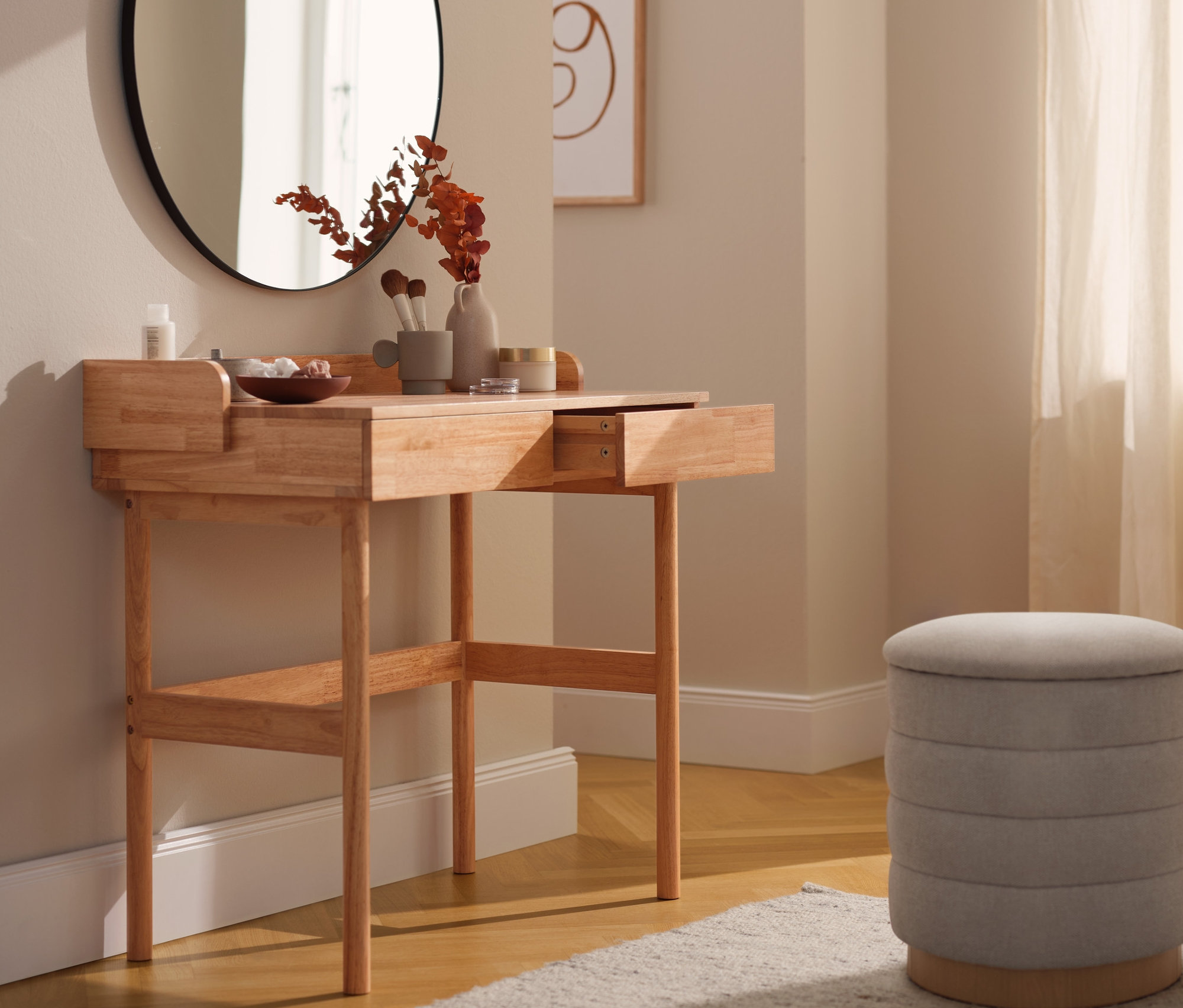 Sminkasztal fiókokkal, kerek tükör és egy bézs színű ülőke egy szobában.