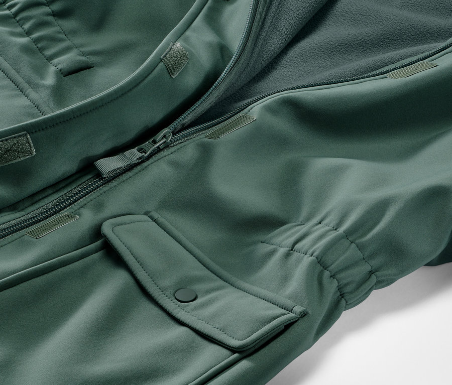 Egy zöld gyerek softshell kabát részlete, nyitott cipzárral és zsebbel.