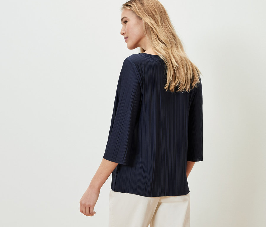 Nő visel egy sötétkék pliszé pólóblúzt.