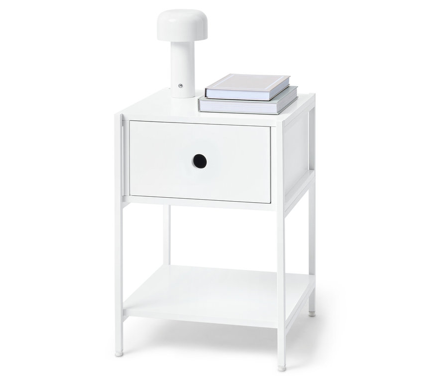 Fehér éjjeliszekrény egy fiókkal, egy lámpával és két könyvvel a tetején.