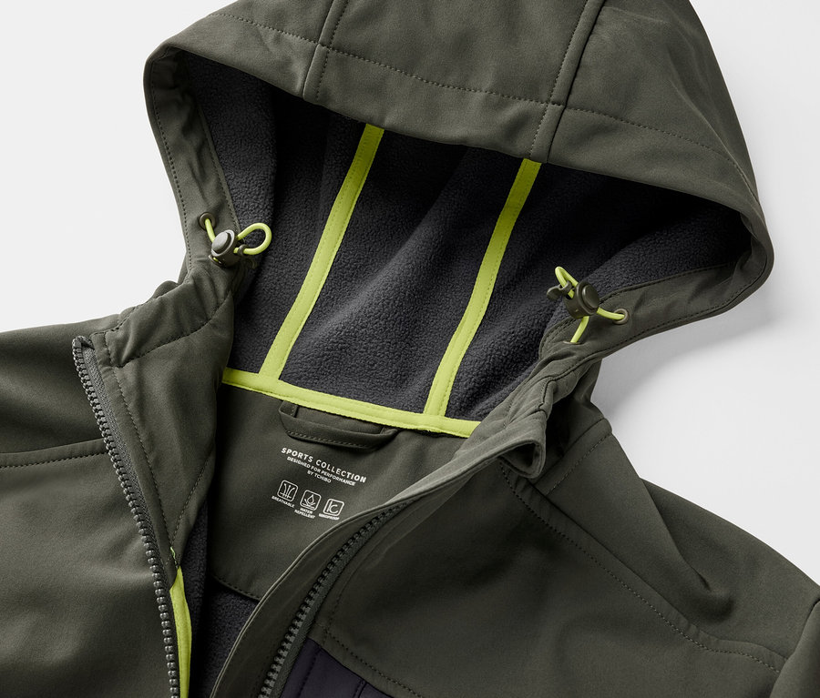 Egy khaki softshell dzseki részlete kapucnival és neon sárga részletekkel.