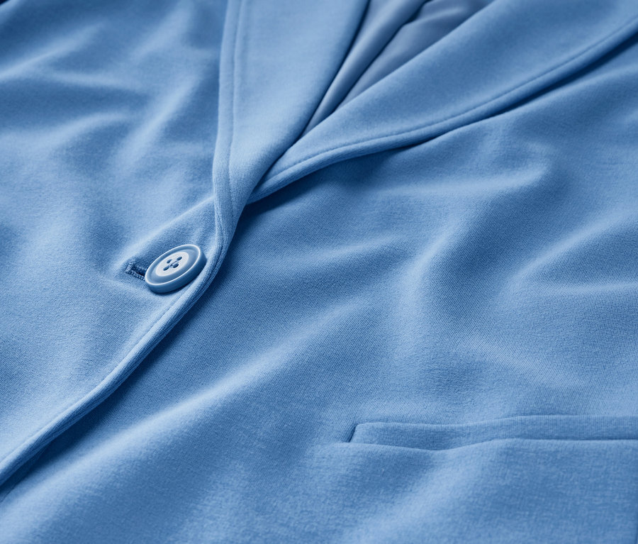 Egy világoskék jersey blézer részlete gombbal és zsebbel.