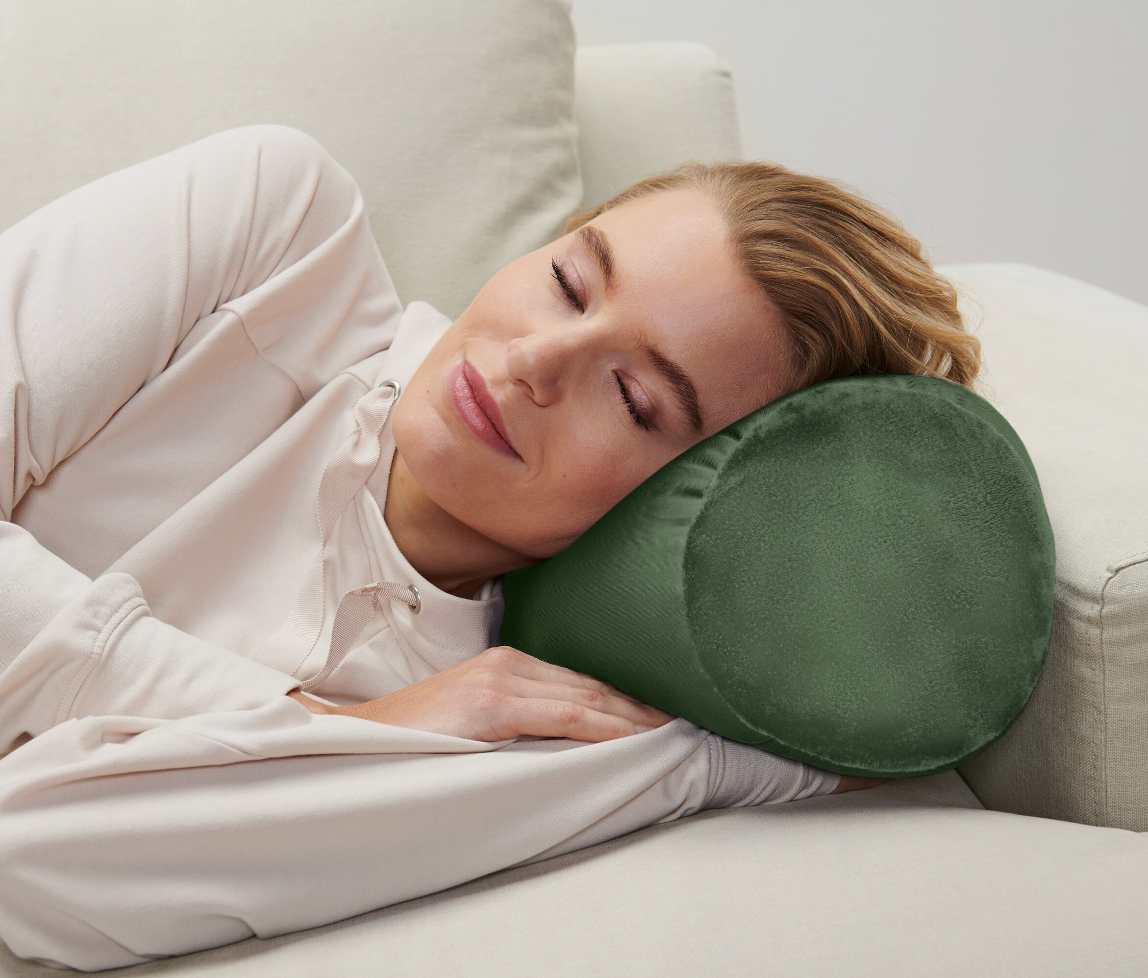 Egy nő alszik a kanapén, hengeres párnával a feje alatt.