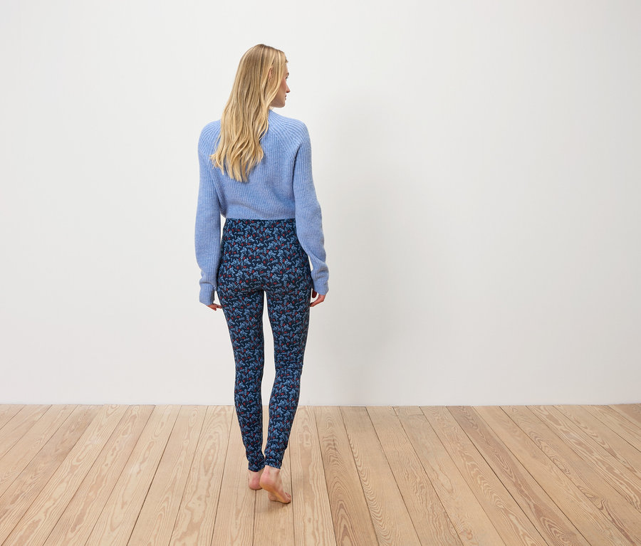 Egy kék pulóvert és mintás leggingst viselő nő háttal áll a kamerának.