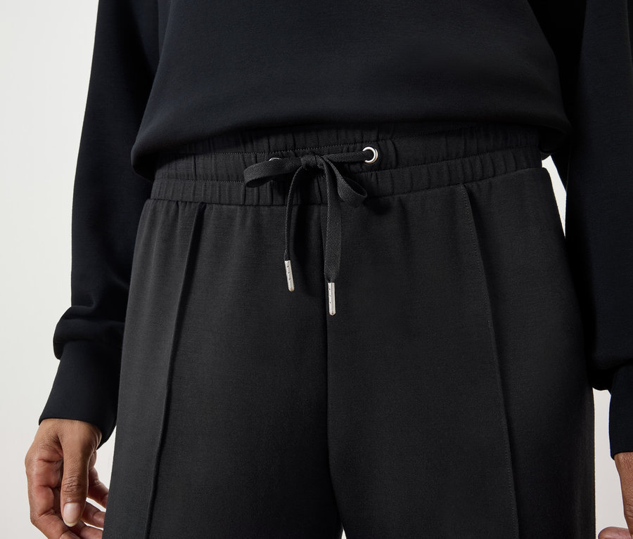 Egy nő részlete, aki fekete, húzózsinóros nadrágot és fekete pulóvert visel.