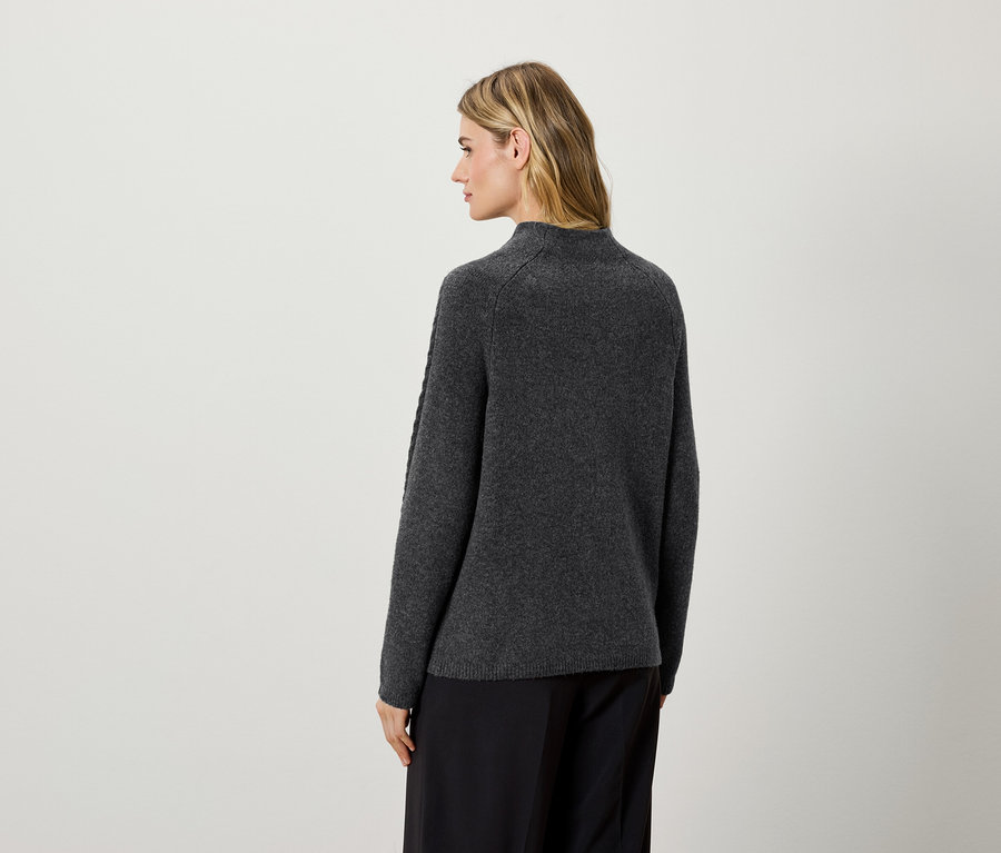 Egy nő háttal a kamerának sötétszürke pulóvert és fekete nadrágot visel.