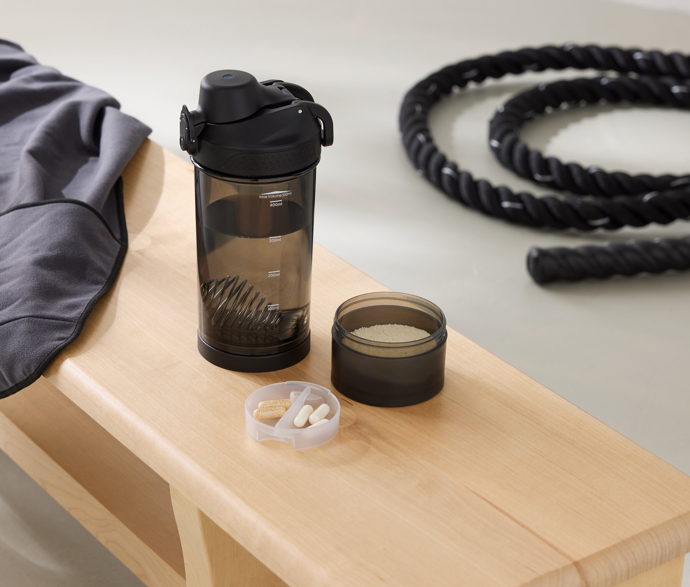 Egy padon szürke pulóver, kulacs, egy doboz por és egy kötél van.