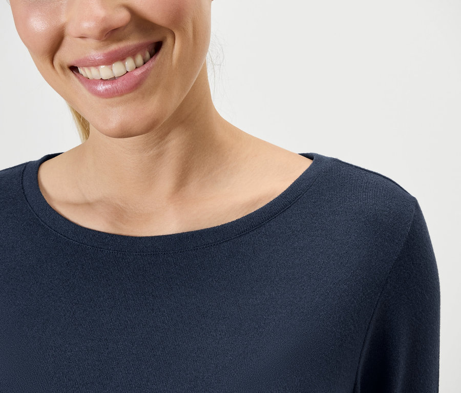 Mosolygó nő sötétkék, hosszú ujjú felsőt visel.