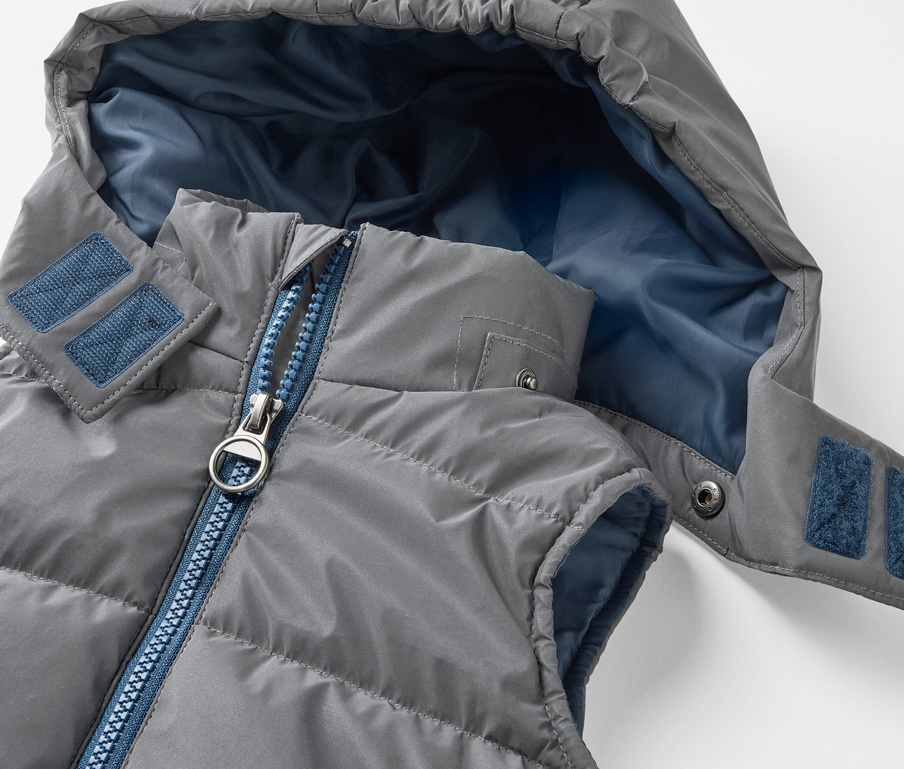 Szürke, steppelt, kapucnis gyerek mellény részlete. A fényvisszaverő steppelt mellény gyerekeknek kék cipzárral és kék kapucni belsővel rendelkezik.