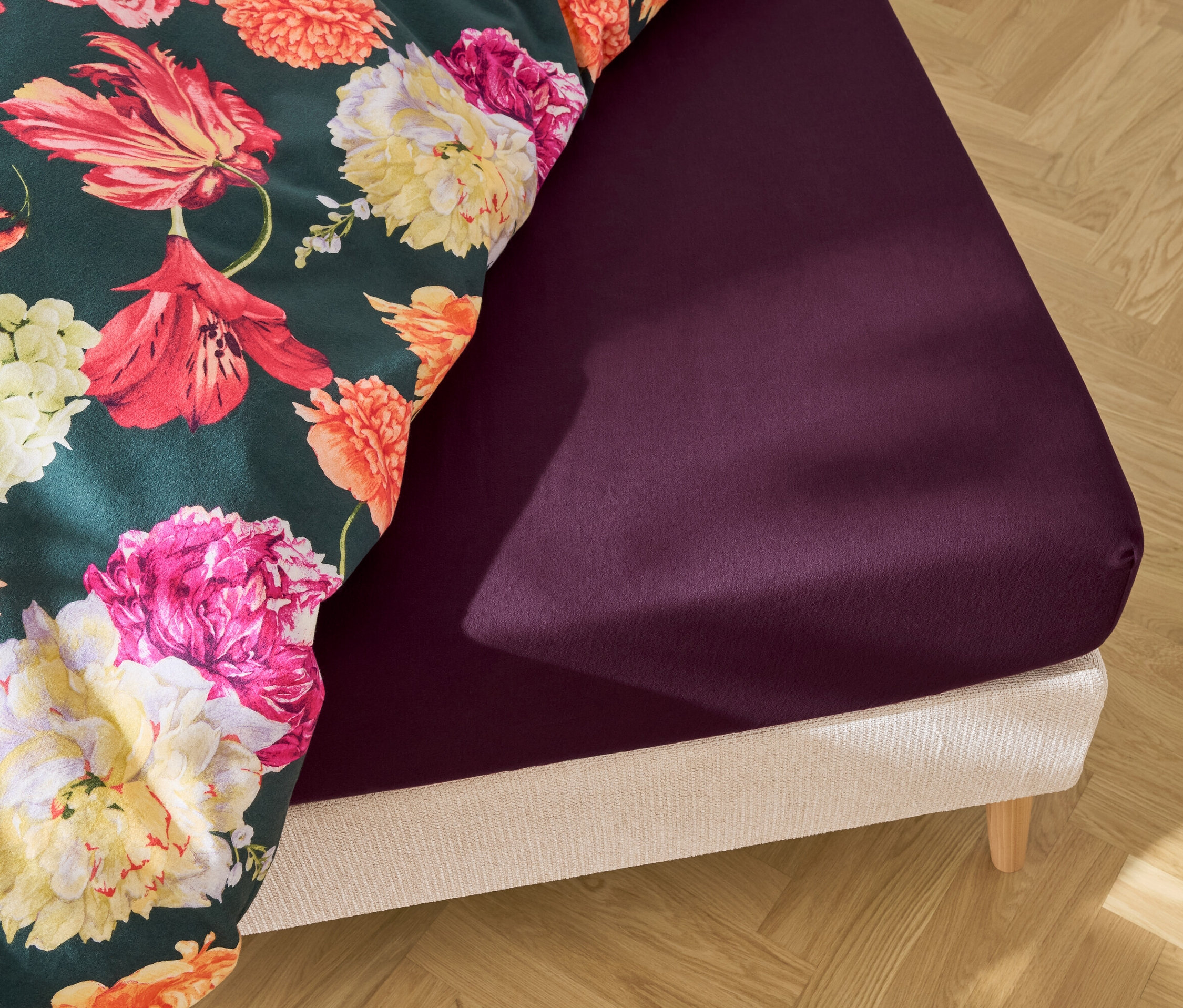 Ágy lila gumis lepedővel és virágos ágyneművel.