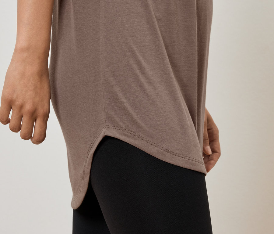 Részleges nézet egy barna tunikát és fekete leggingset viselő nőről.
