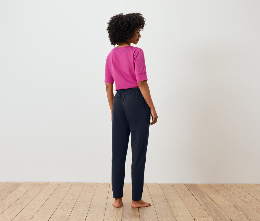 Hátulnézet egy afro frizurás nőről, aki rózsaszín pólót és sötétkék nadrágot visel.