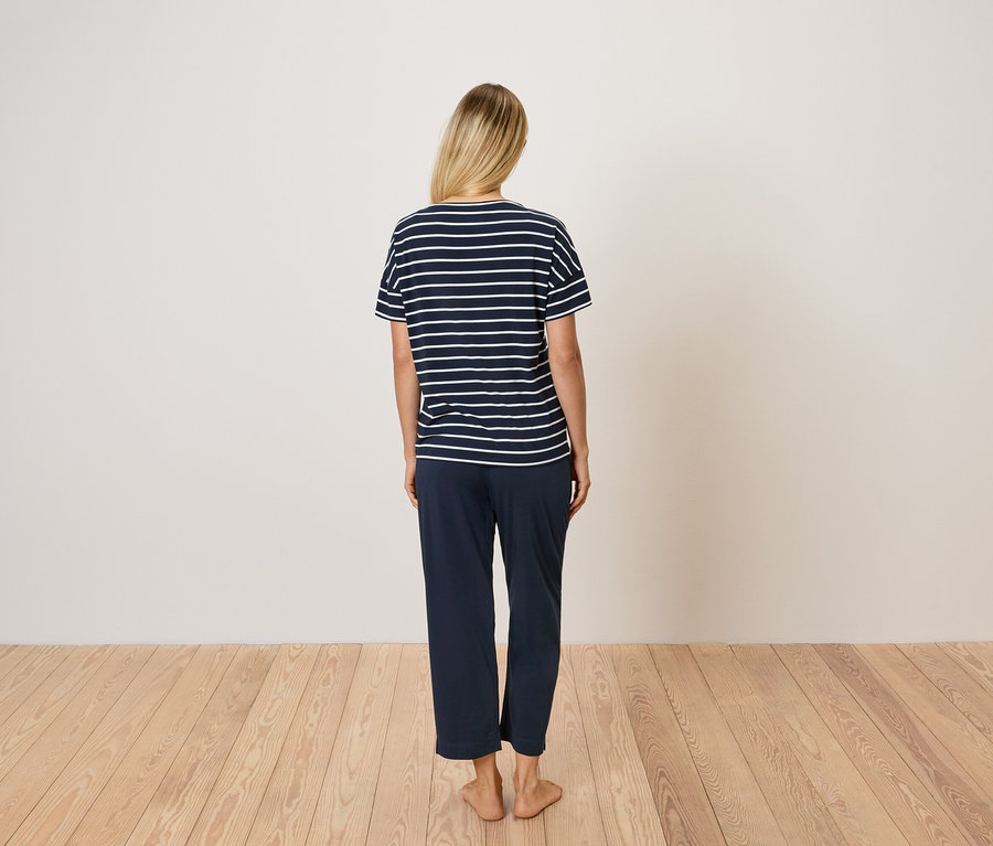 Hátulról látható egy szőke hajú nő, aki kék csíkos pólót és kék nadrágot visel.