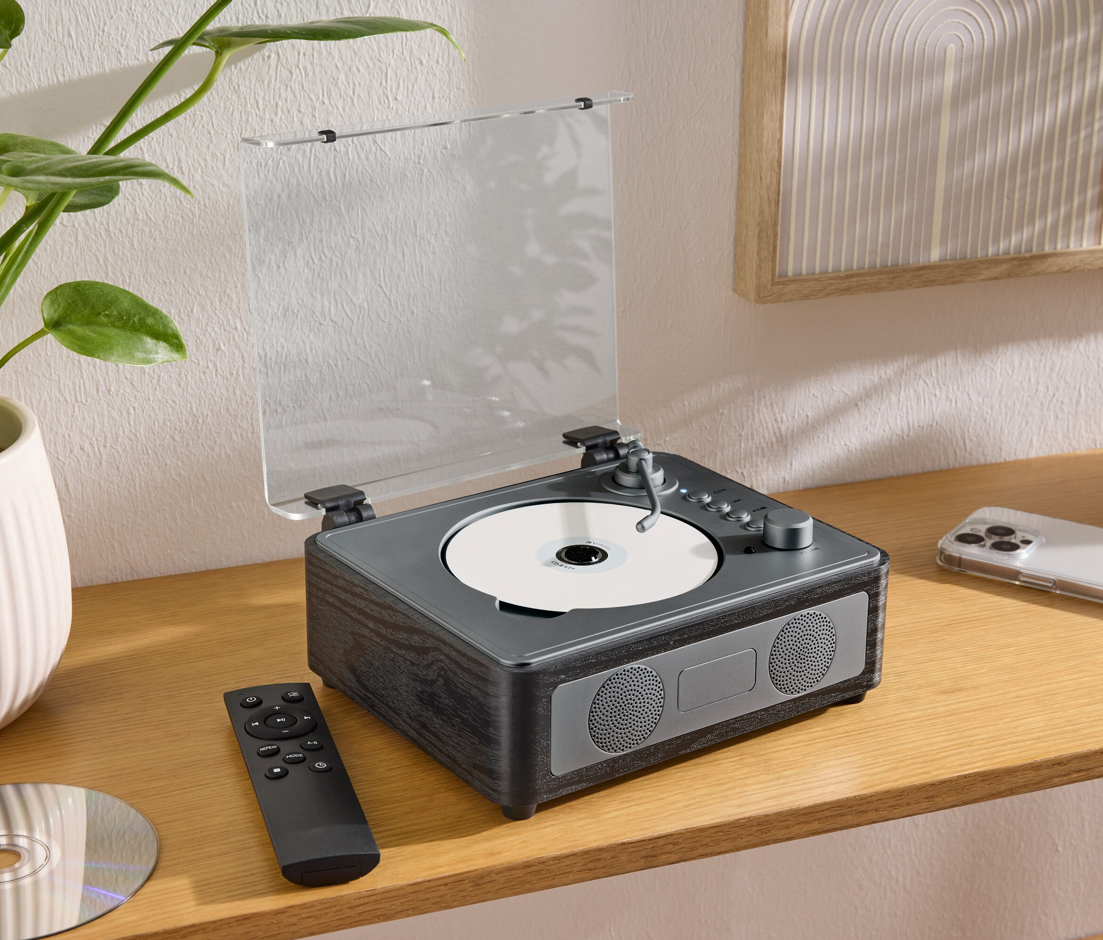 Az asztalon egy CD/Bluetooth® hangszóró áll CD-vel, távirányítóval és mobiltelefonnal.