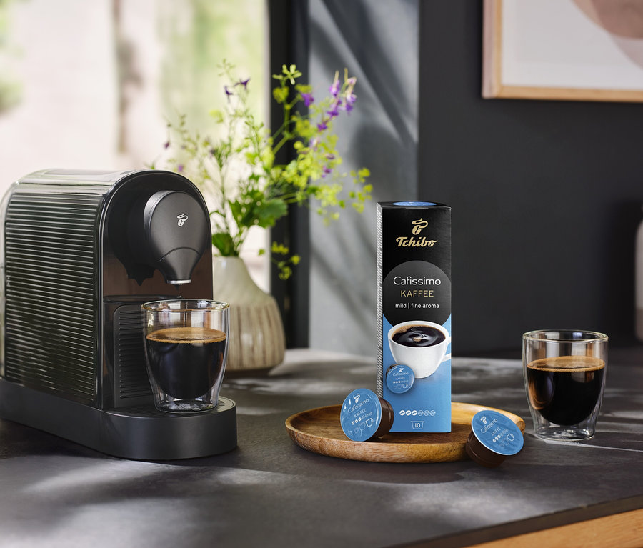 Kávéfőző egy csésze kávé és egy csomag 10 db-os Caffè Fine kávékapszula mellett.