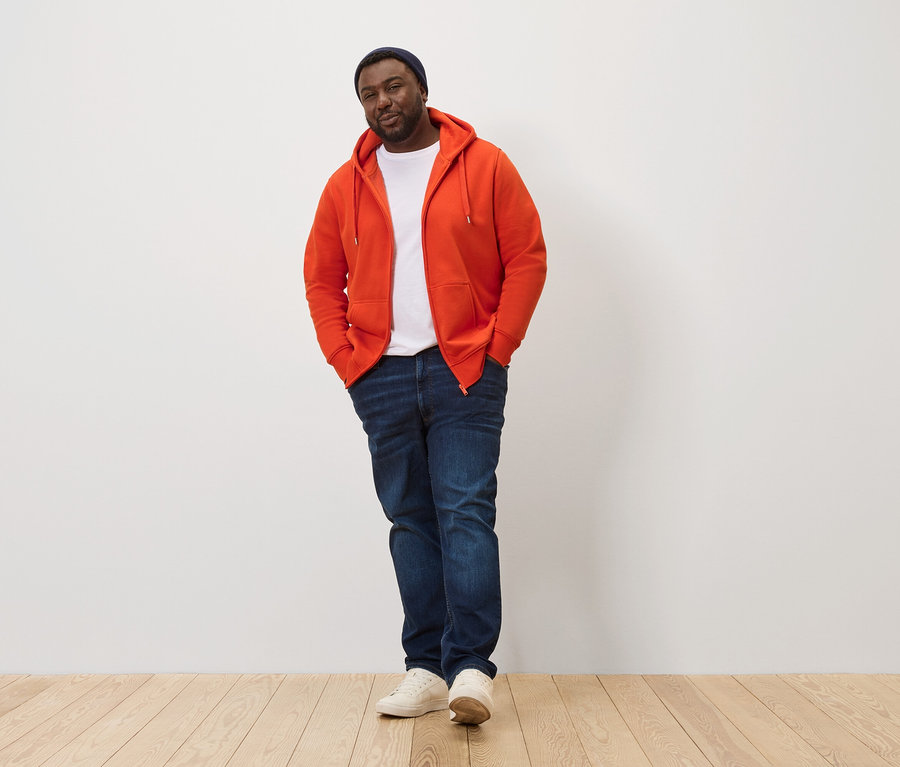 Férfi pózol narancssárga kapucnis felsőben.