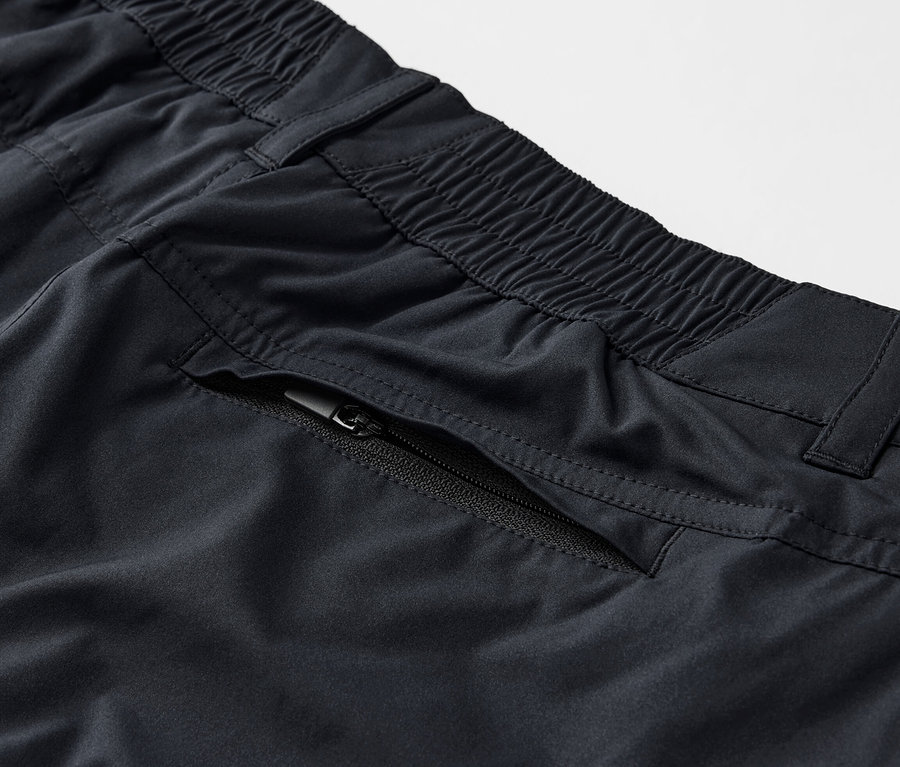 Egy fekete, 2 az 1-ben funkcionális nadrág részlete cipzáras zsebbel.