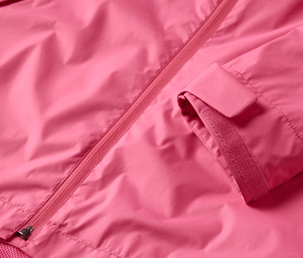 Egy rózsaszín esőkabát részlete, cipzárral és ujjal.
