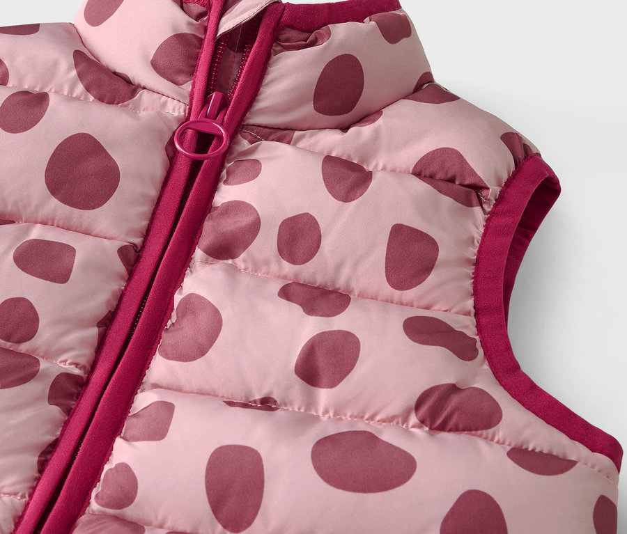 Részlet egy rózsaszín, steppelt mellényről bordó pöttyökkel és cipzárral.