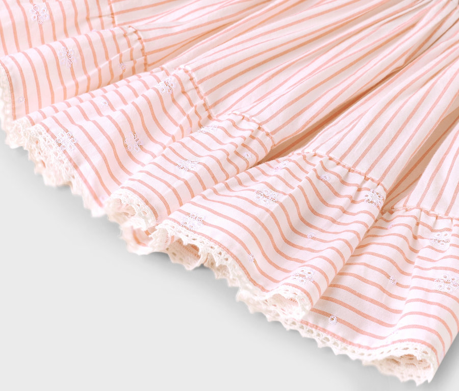 Egy rózsaszín csíkos, csipkés szegélyű szoknya szegélyének közeli képe.