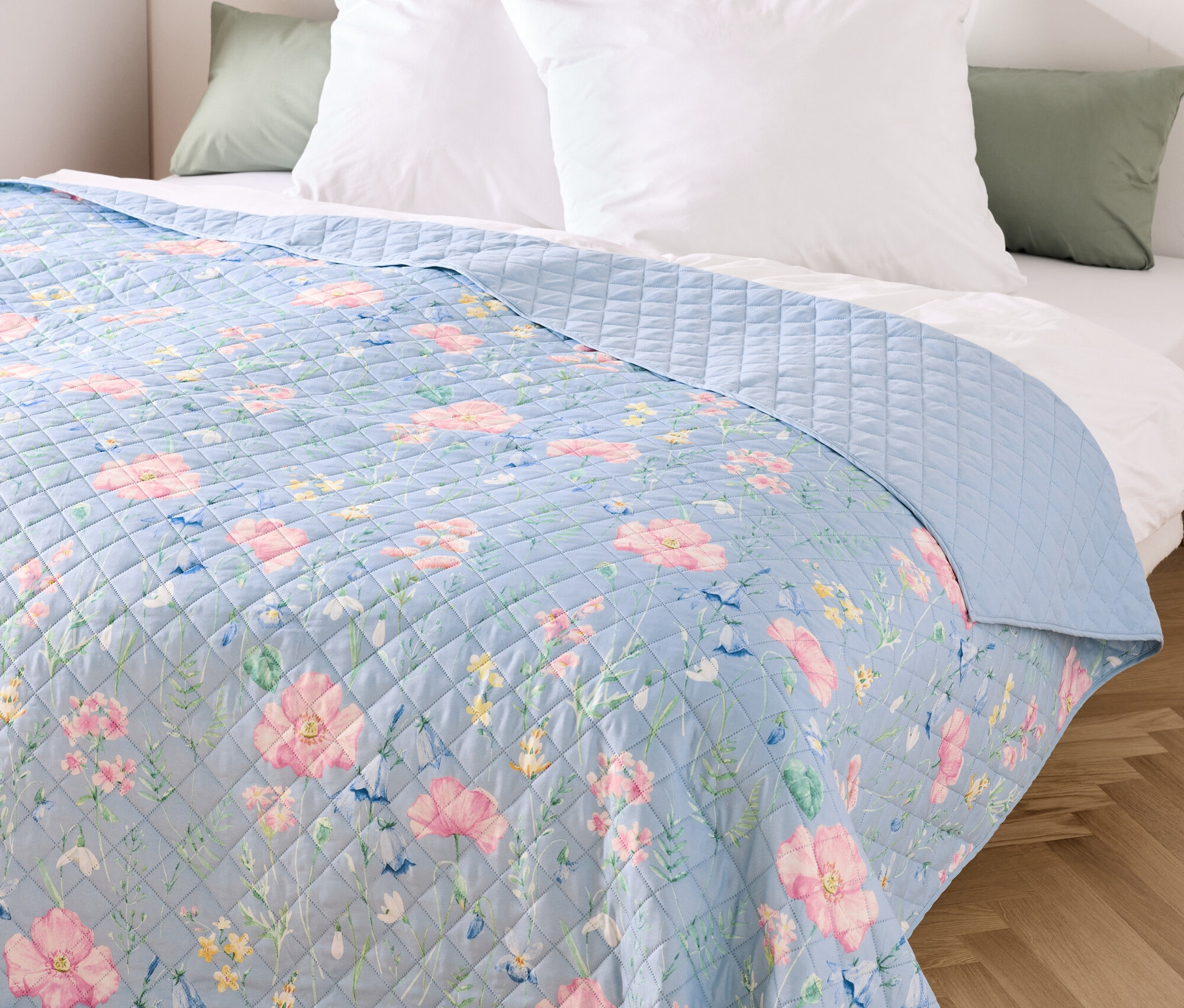 Virágmintás kék ágytakaró fehér párnákkal az ágyon.