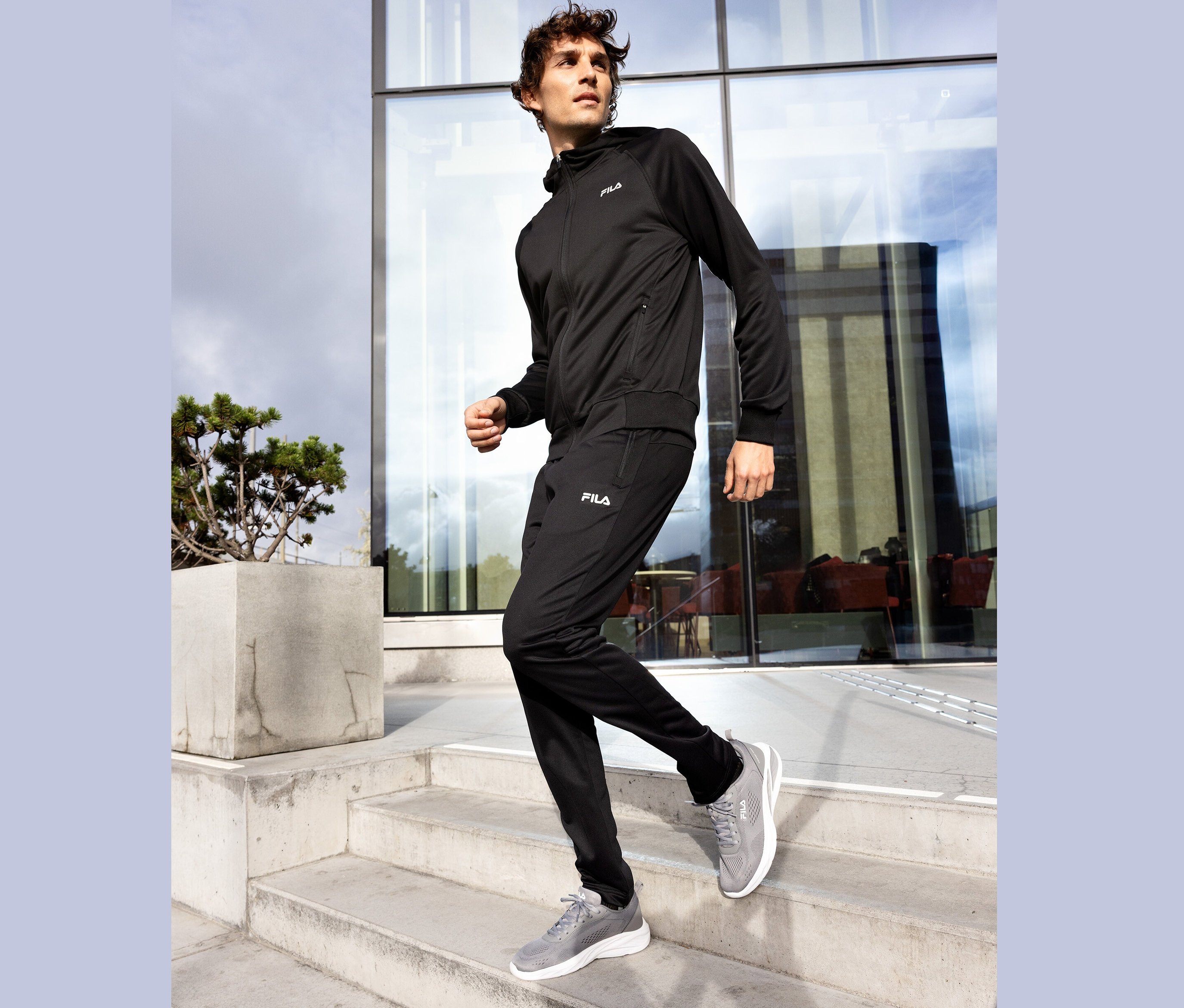 Férfi fekete Fila tréningruhában és szürke tornacipőben megy le egy beton lépcsőn.