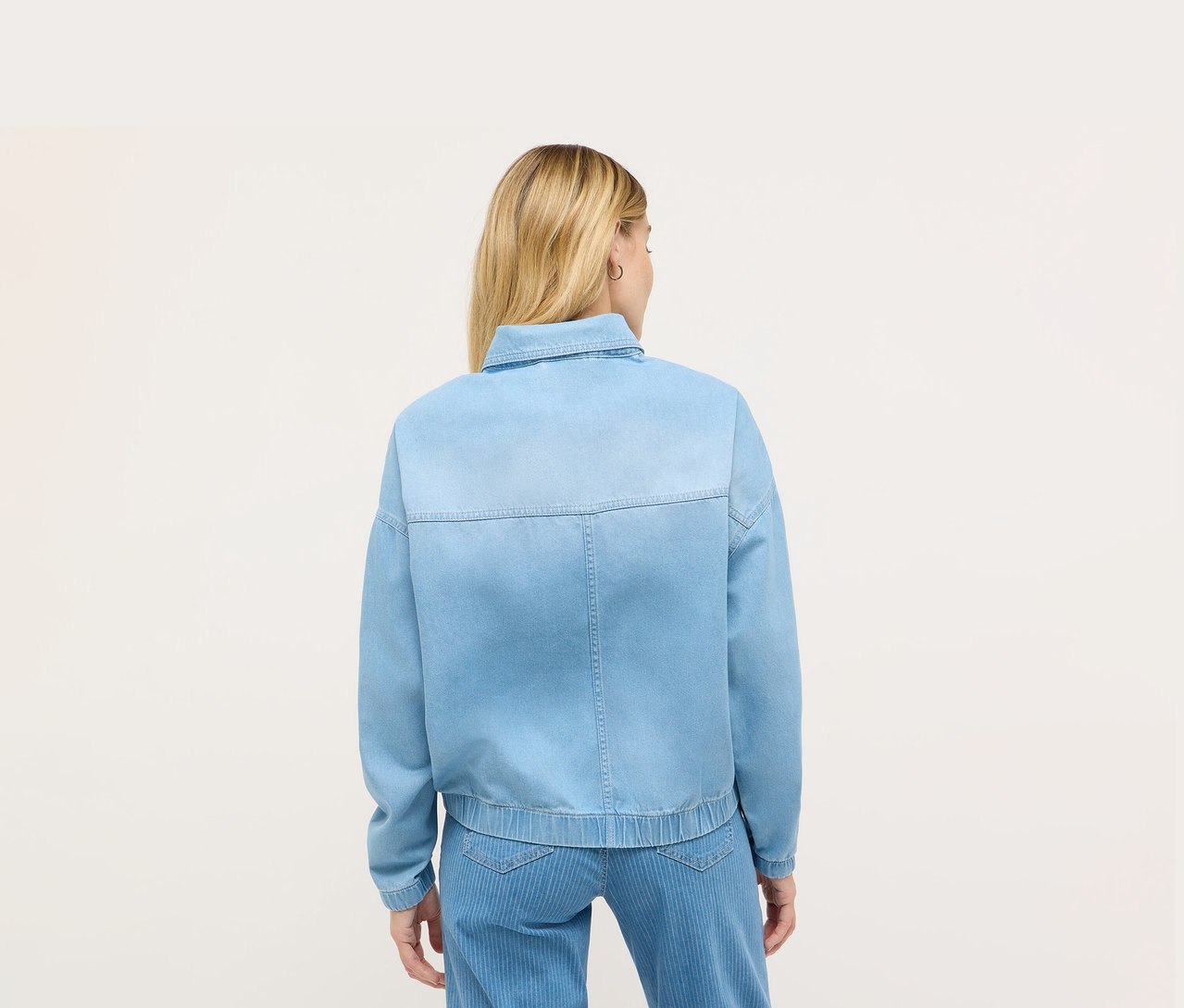 Hátulnézetből egy szőke hajú nő kék Angels farmerdzsekiben.