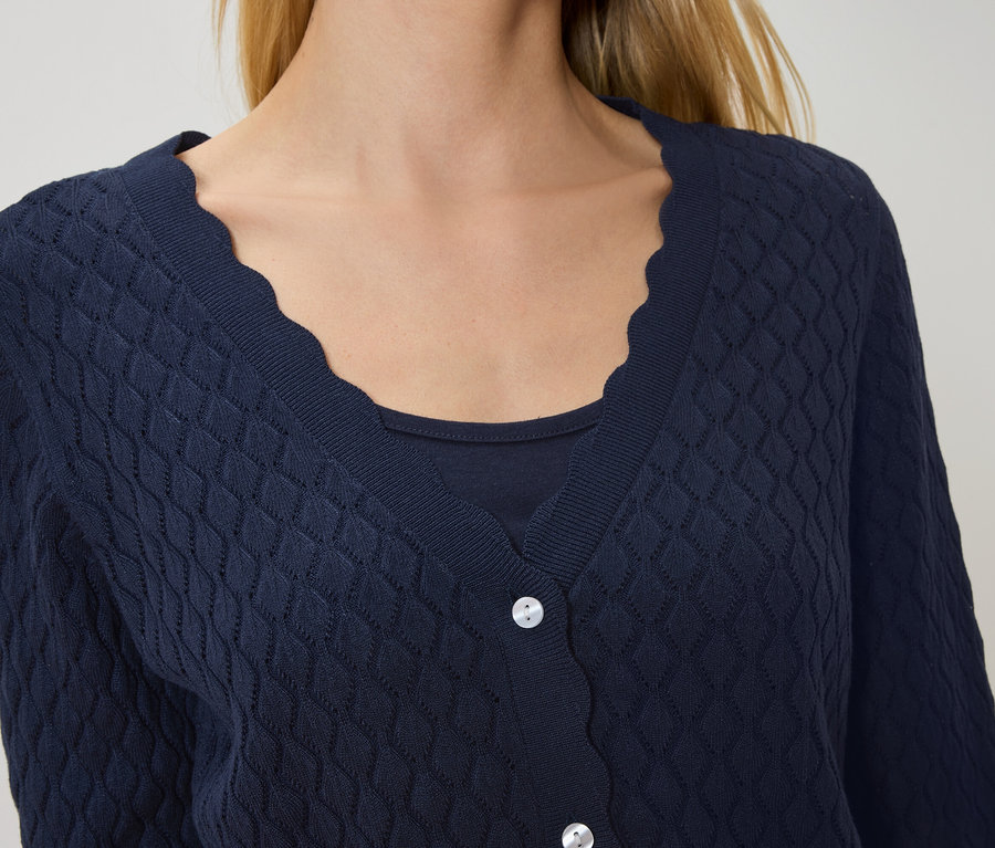 Nő visel egy hullámos szegélyű, sötétkék kardigánt egy sötétkék felső felett.
