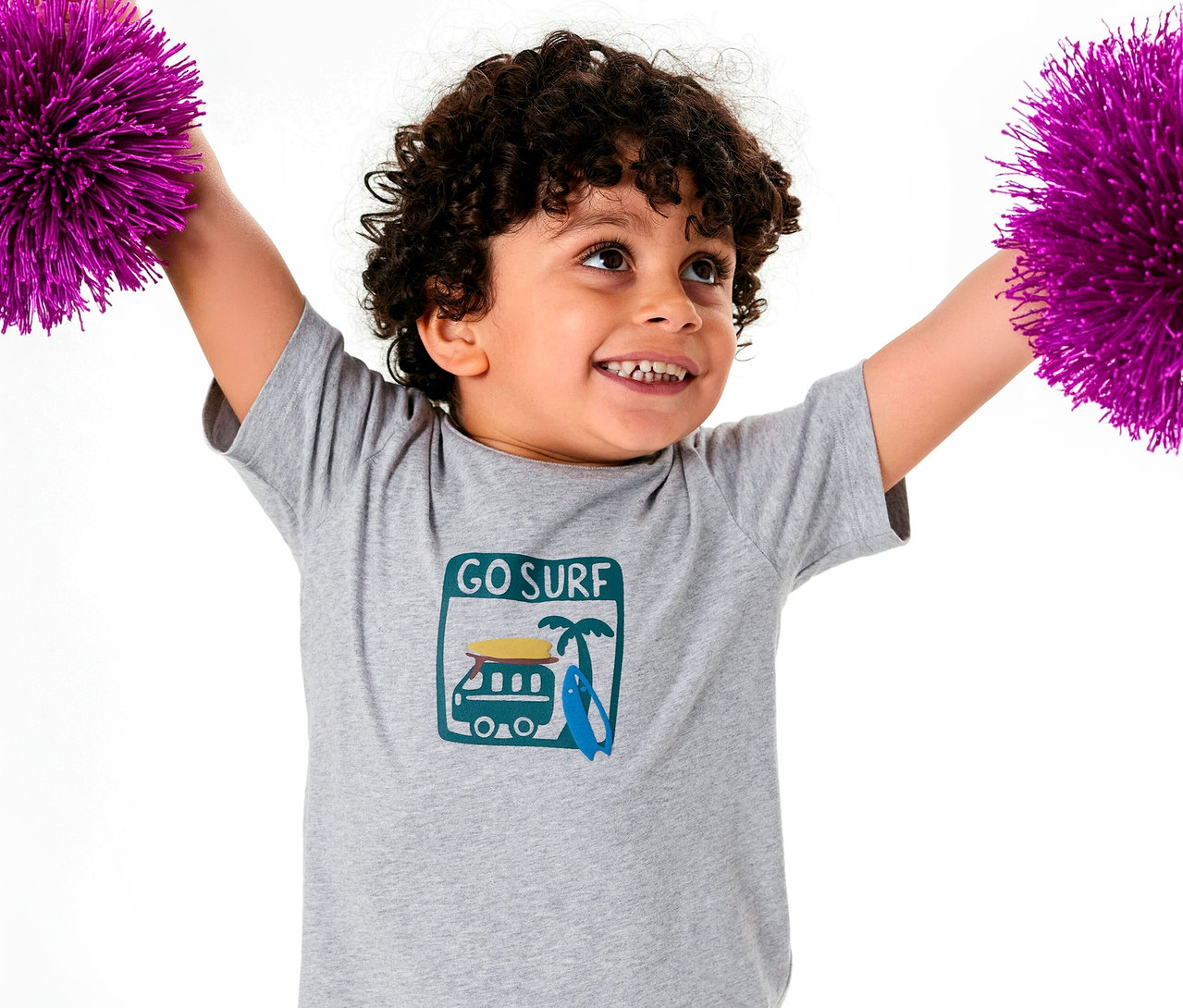 Göndör hajú fiú SCHIESSER rövidnadrágos gyerekpizsama felsőt visel, lila pomponokat tart a magasban.