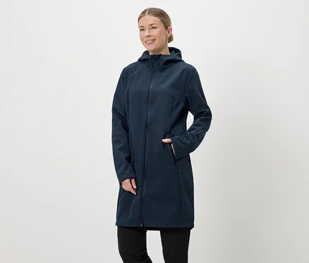 Nő sötétkék, hosszú softshell kabátban, kapucnival és cipzárral, kezét a zsebébe teszi.