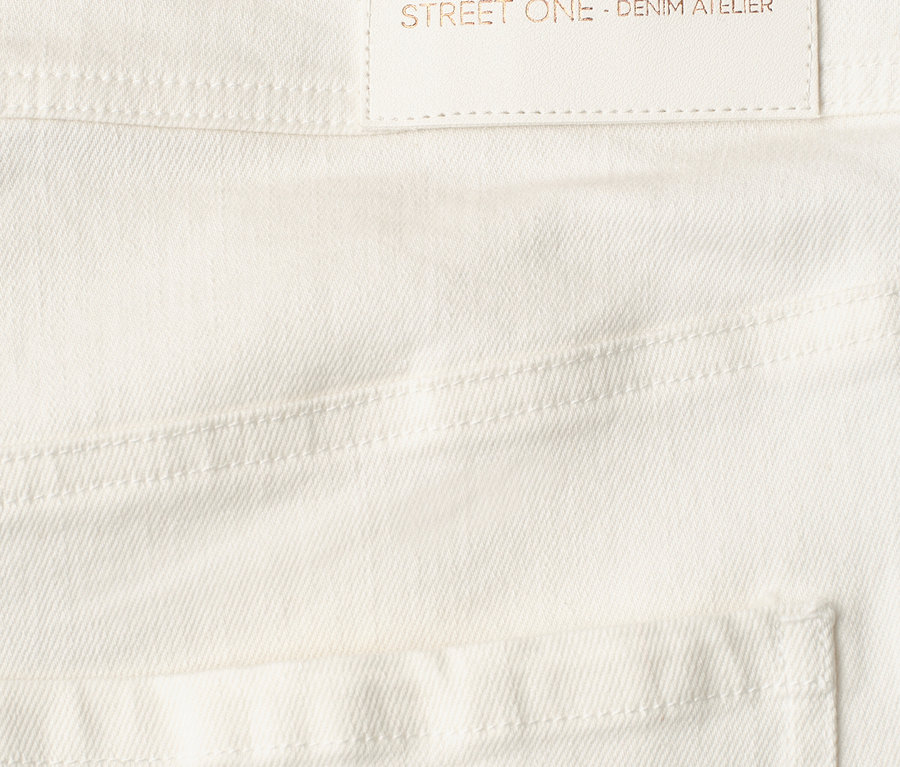 Fehér Street One Jeans közelképe, világos címkével, amelyen a 'designed with passion STREET ONE - DENIM ATELIER' felirat látható.