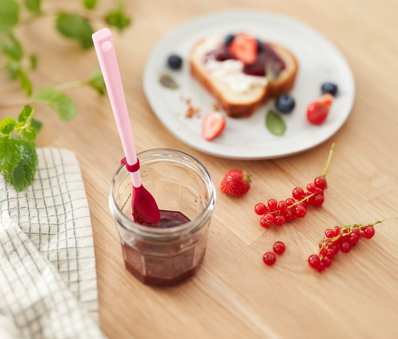 Lekváros üveg rózsaszín kanállal, pirítós eperrel és áfonyával, valamint ribizli egy fa asztalon.