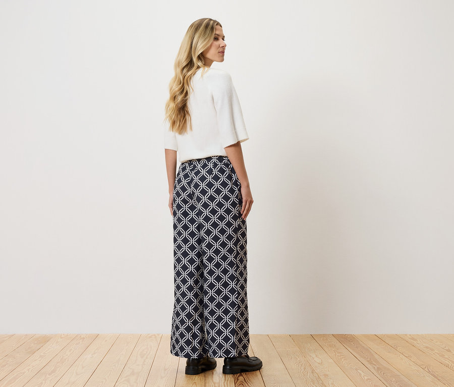 Nő fehér felsőt és fehér geometriai mintás, hosszú, sötétkék nadrágot visel.