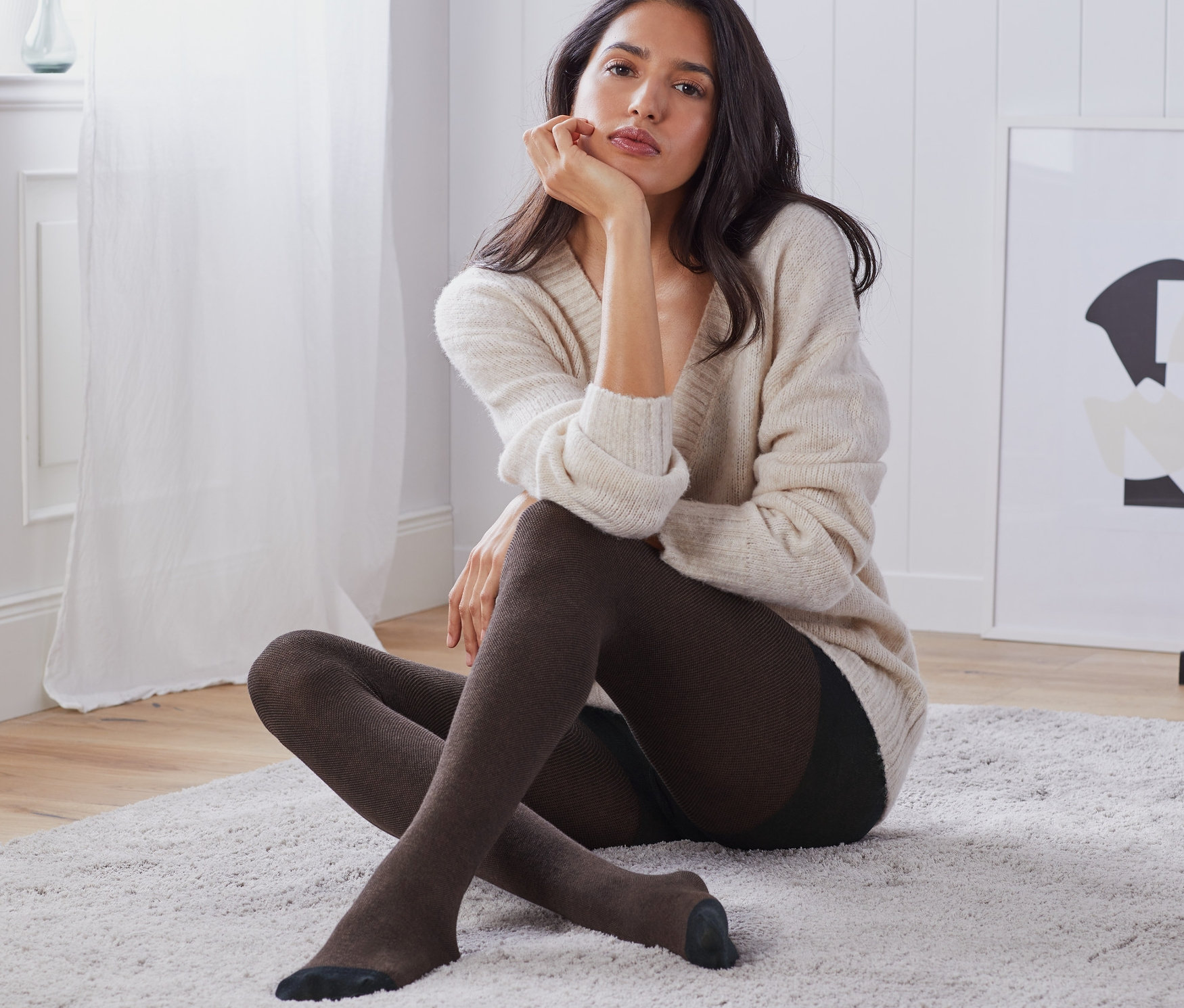 Egy nő ül a szőnyegen és barna női strukturált harisnyát visel.