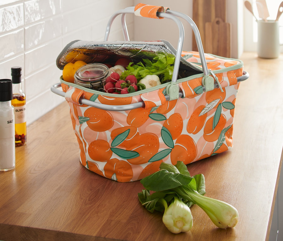 Egy barack mintás, ételekkel teli, összecsukható hűtőkosár áll a konyhapulton.