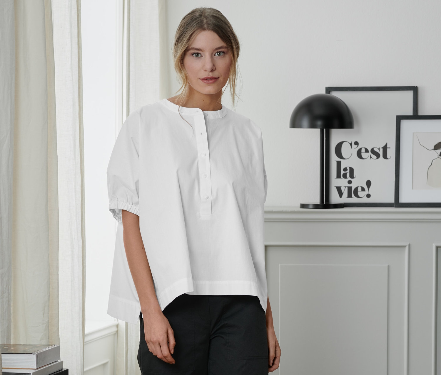 Nő áll fehér, rövid ujjú poplin blúzban és fekete nadrágban.