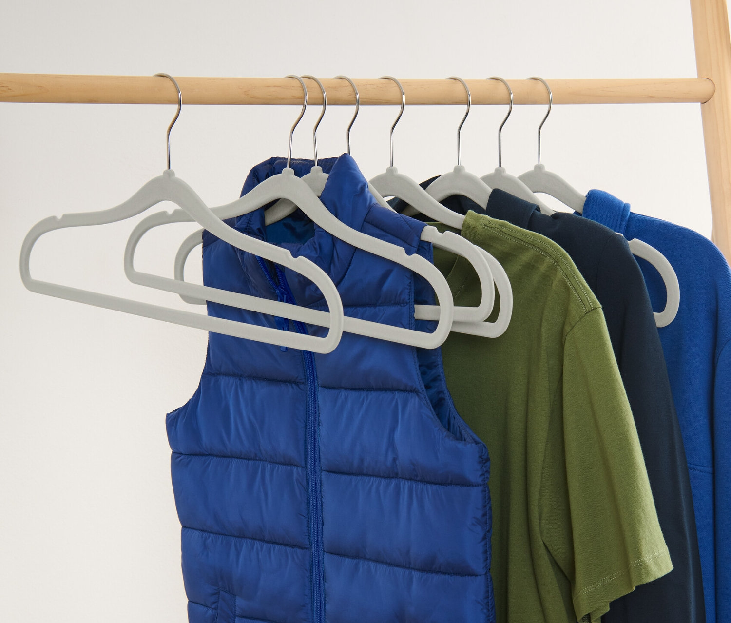 Egy kék mellény és színes ruhák lógnak 8 keskeny vállfán.