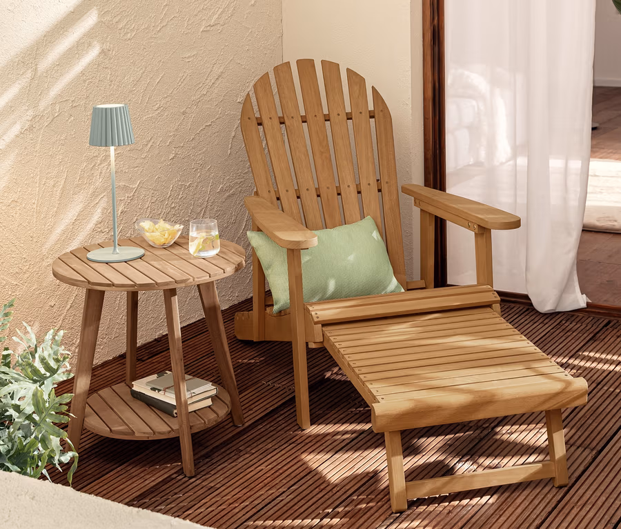 Egy Adirondack kerti szék kihúzható lábtartóval egy „Lenja” 2 szintes oldalasztal mellett áll, melyen két zsályazöld LED-es akkus asztali lámpa található.