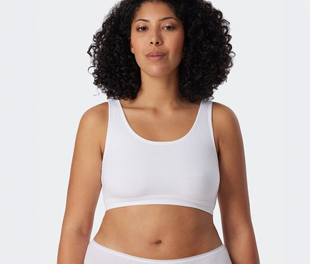Göndör hajú nő visel egy fehér SCHIESSER bustier melltartót és fehér alsóneműt.
