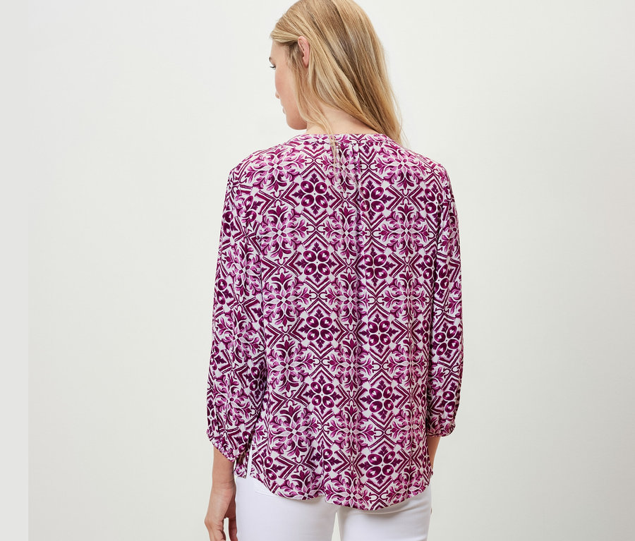 Hátulnézet egy nőről, aki Női 7/8-os ujjú tunikablúzt visel, mintás, fukszia, és fehér nadrágot.