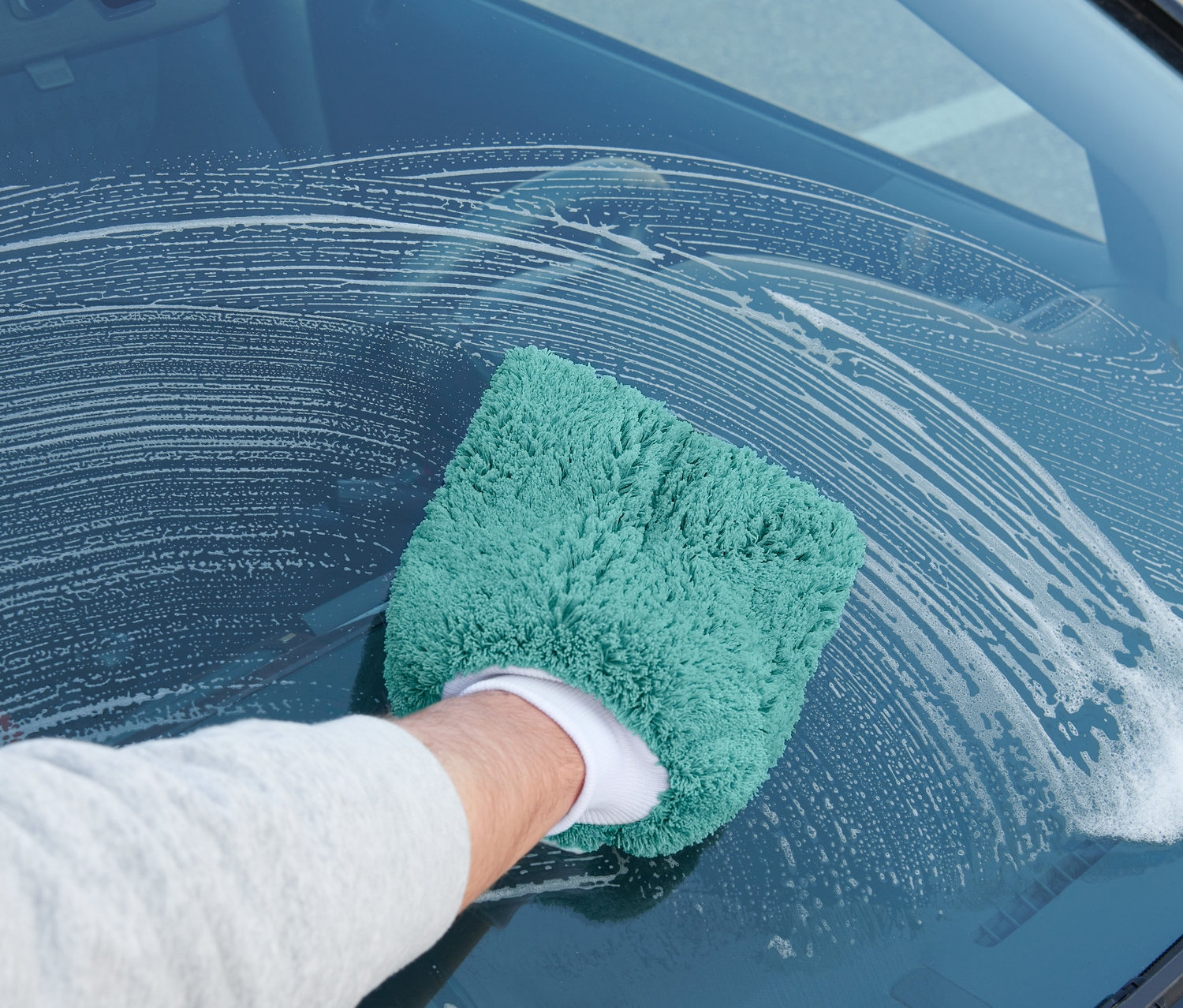 Egy férfi autótisztító kesztyűvel tisztítja az autó szélvédőjét.