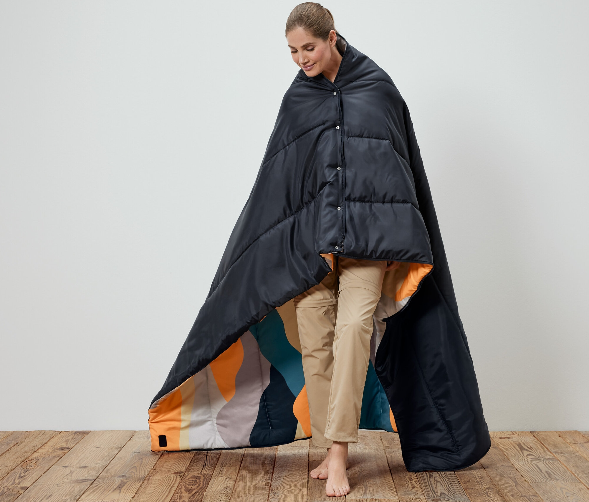 Nő fekete 4 az 1-ben hálózsákba burkolózva. A hálózsák belseje mintás.