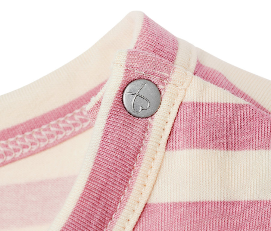 Közelkép egy rózsaszín és krémszínű csíkos, szív alakú, ezüst gombbal ellátott kisgyerek dzsörzéruháról.