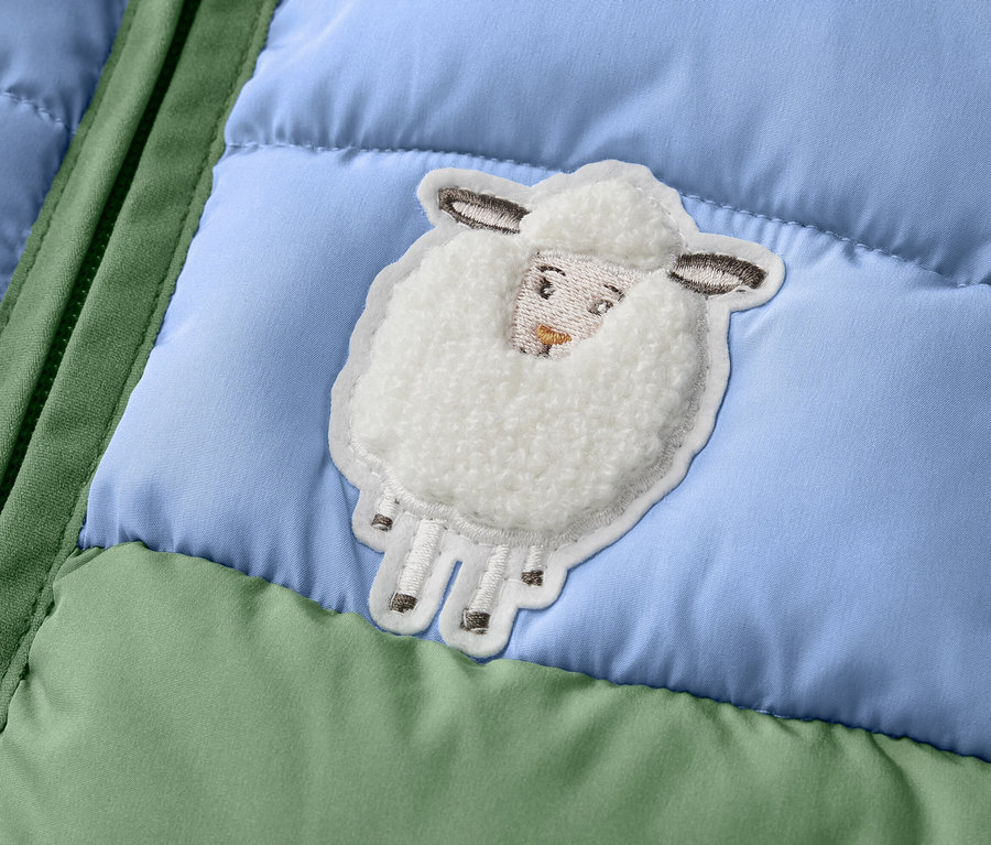 Részlet egy zöld/kék színösszeállítású, bárányka mintás kisgyerek steppelt mellényből.