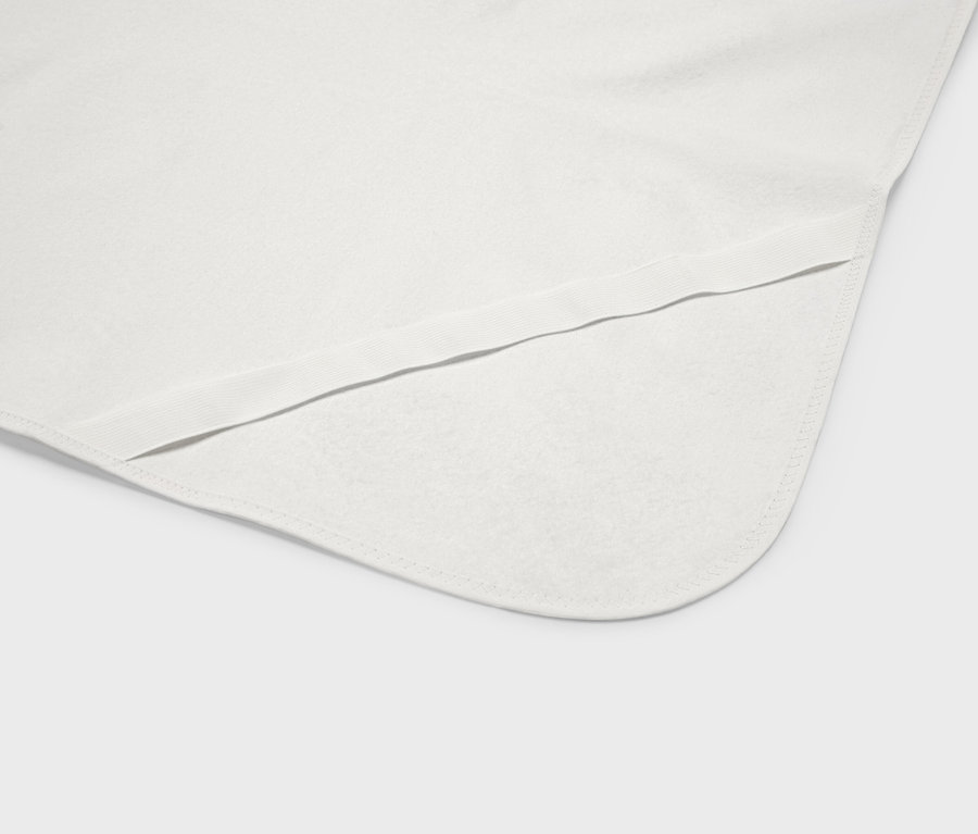 Egy fehér babatakaró közeli képe lekerekített sarkokkal és elasztikus szegéllyel.