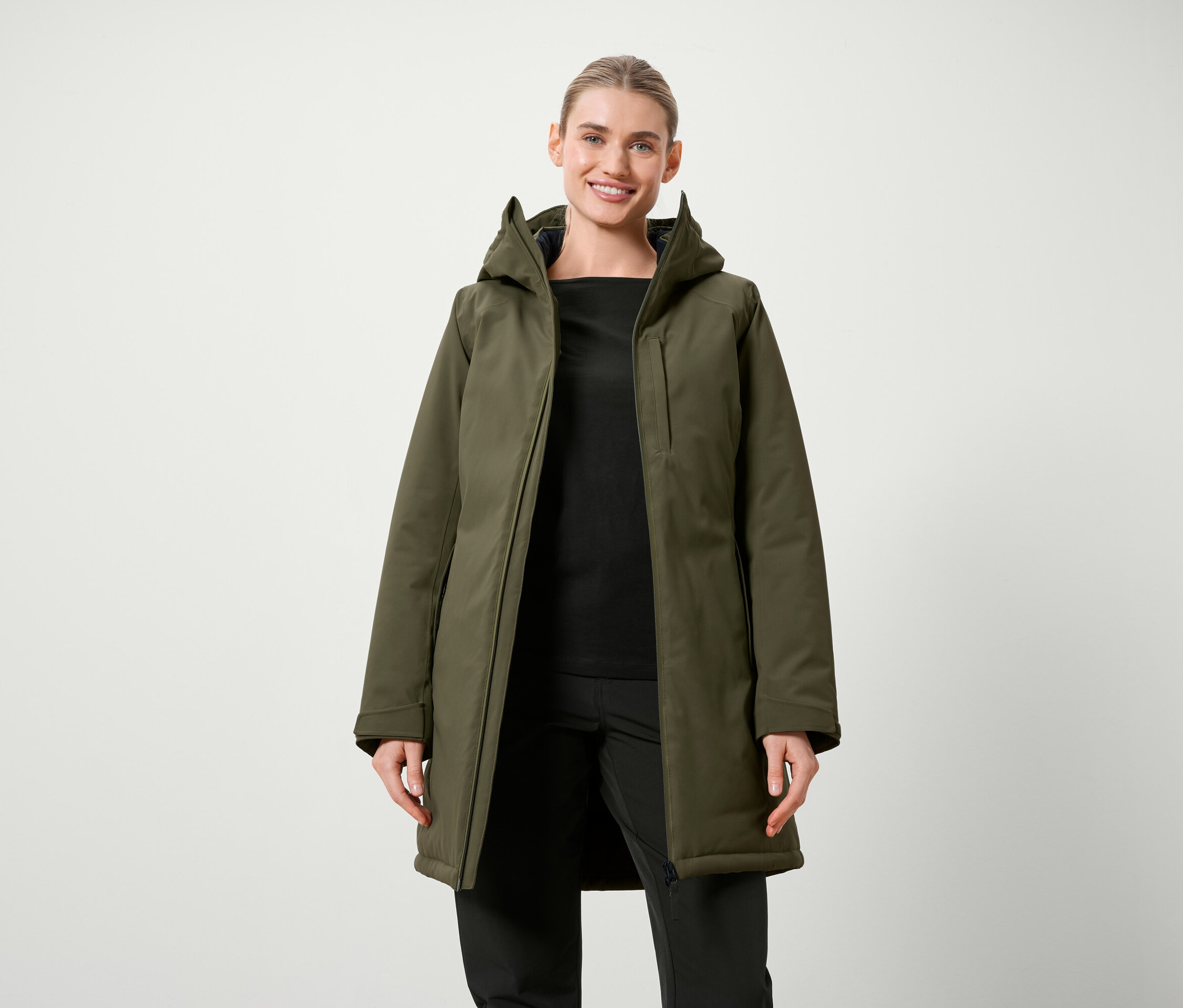 Nő pózol olívazöld, kapucnis kabátban, fekete ruhában.