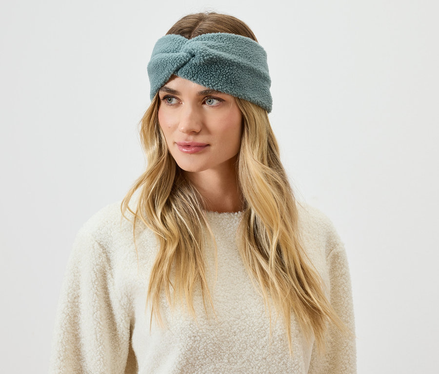 Portré egy szőke hajú nőről, aki kékeszöld, bozontos fejpántot visel.