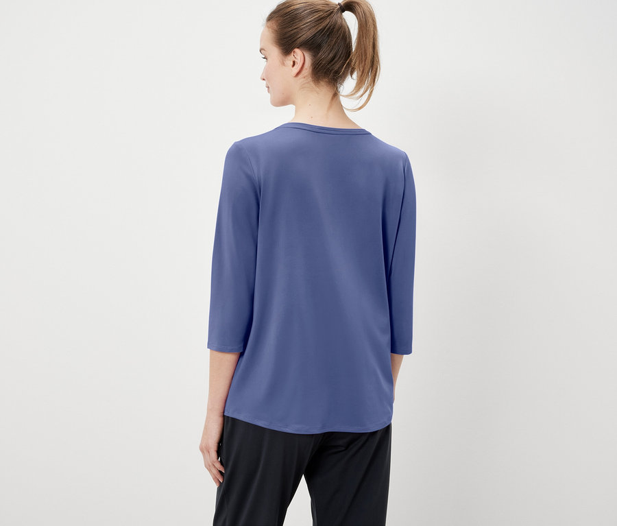 Hátulnézet egy lófarokba kötött hajú nőről, aki kék, háromnegyedes ujjú pólót és fekete nadrágot visel.