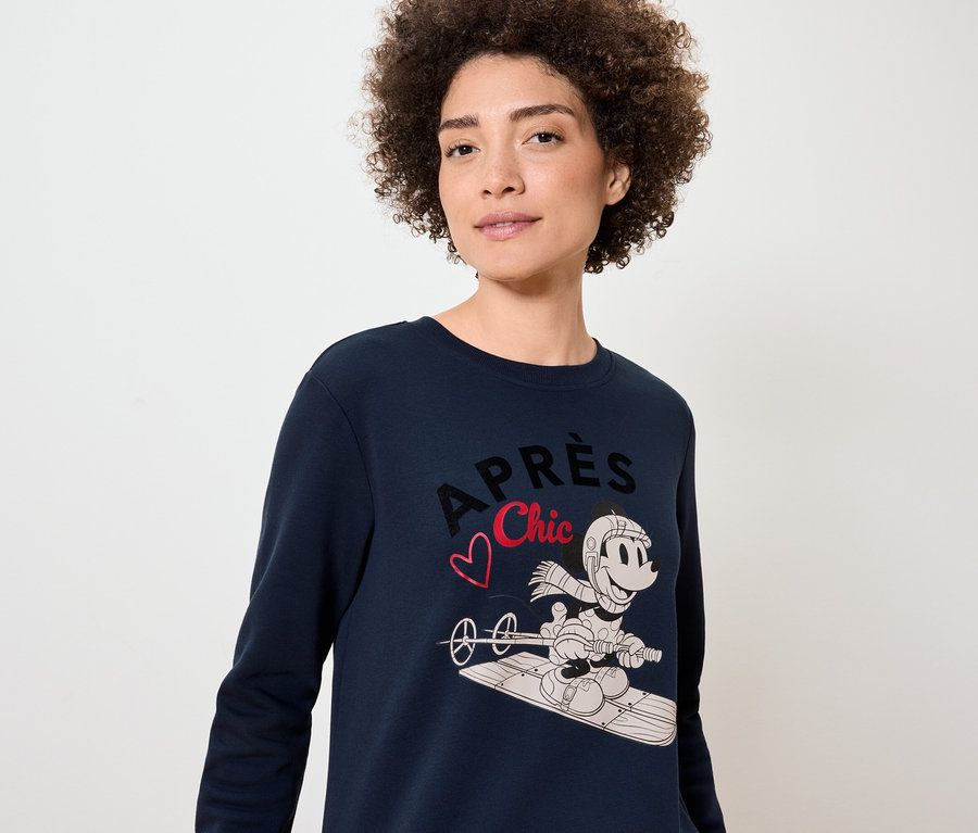 Egy nő sötétkék pulóvert visel, amelyen egy hódeszkázó Mickey egér látható.