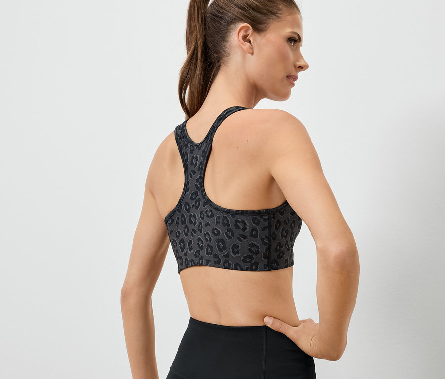 A kamerának háttal álló nő állatmintás sportmelltartót és fekete leggingst visel.
